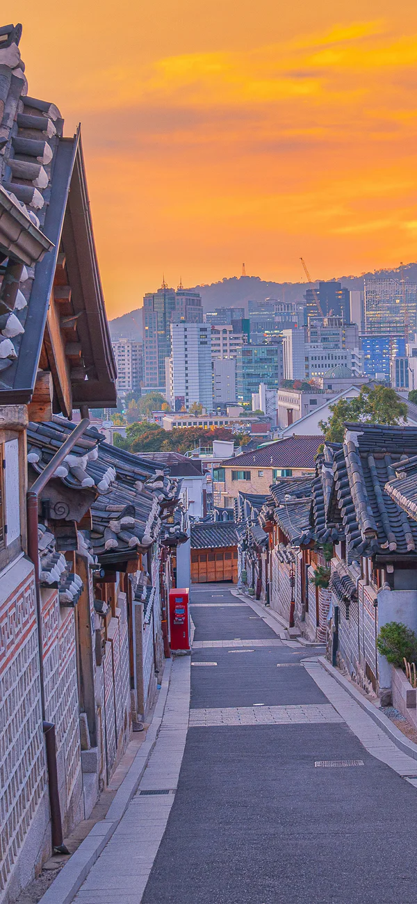 Sonnenuntergang über dem Bukchon-Hanok-Dorf in Seoul, Südkorea, mit der Skyline der Stadt im Hintergrund