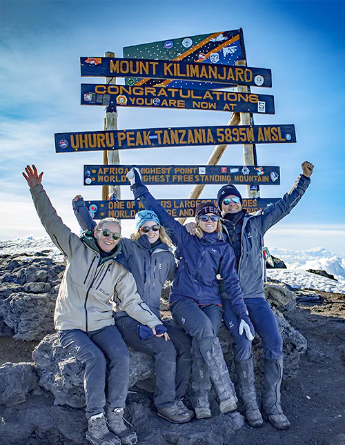 Familie sitzt vor dem Schild am Uhuru Peak auf dem Gipfel des Kilimandscharo