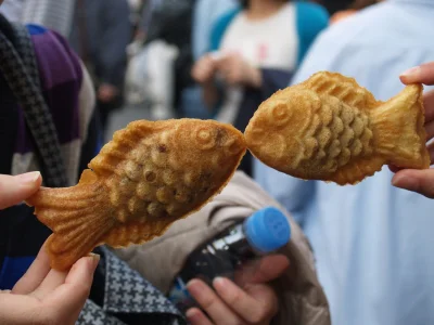 Zwei Personen halten Taiyaki-Waffeln hoch, sodass die Fische aussehen, als würden sie sich küssen