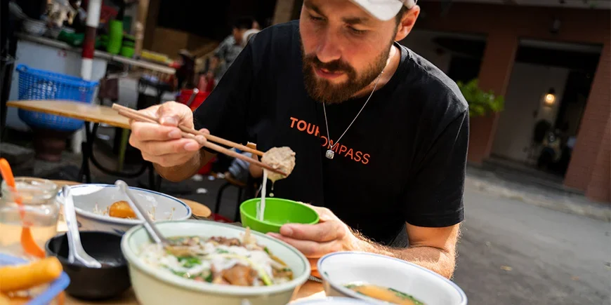 Mann im TourCompass-T-Shirt beim Essen an einem Straßenimbiss in Vietnam