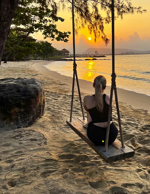 Eine Person sitzt auf einer Schaukel am Strand und genießt den Sonnenuntergang
