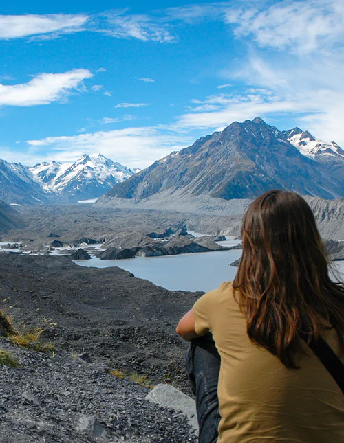 Eine Person bewundert die schneebedeckten Berge und den wunderschönen Gletschersee im Aoraki/Mount-Cook-Nationalpark