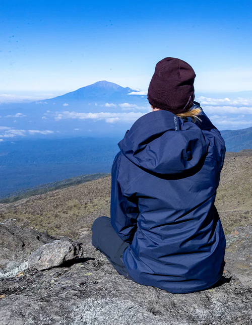 Frau sitzt auf einem Berggipfel und bewundert die Aussicht