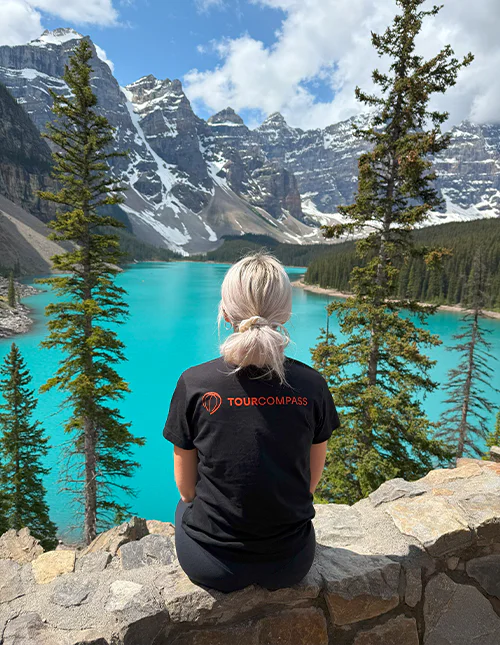 Eine Frau im TourCompass-T-Shirt blickt auf einen türkisfarbenen See und schneebedeckte Berge in Kanada