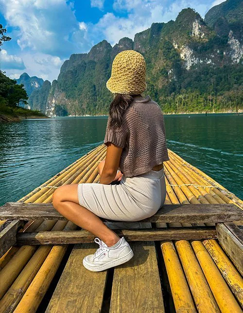 Eine Frau gleitet auf einem Bambusfloß über einen thailändischen See, umrahmt von spektakulären Kalksteinbergen.