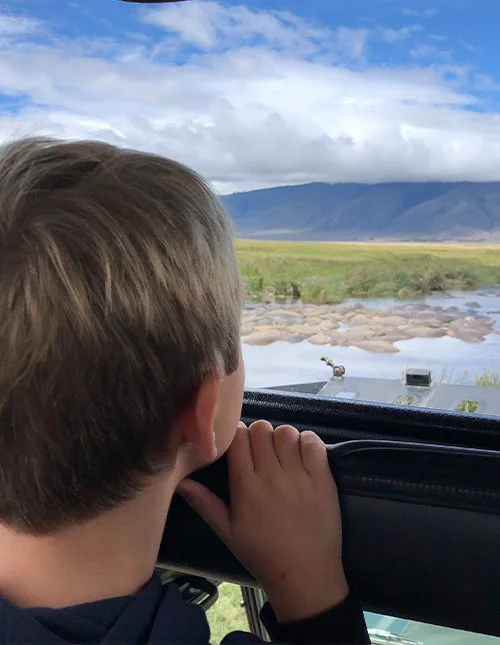 Ein Kind blickt aus einem Safarifahrzeug auf einen Fluss und die Savanne