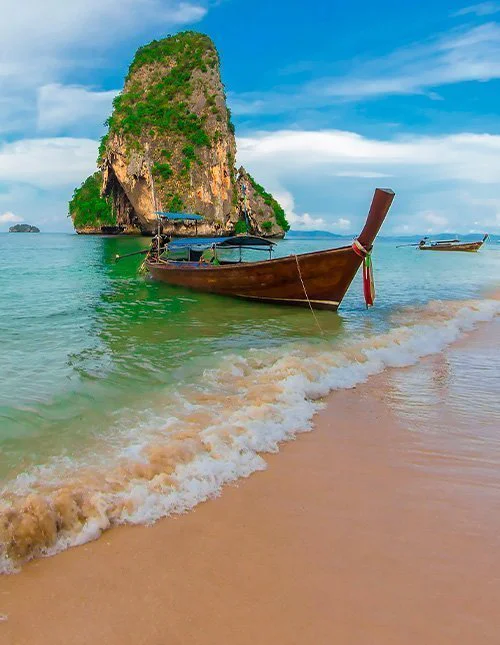 Longtail-Boot an einem tropischen Strand und einem Kalksteinfelsen im kristallklaren Wasser
