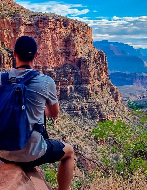 Ein Mann steht auf einem Felsen entlang des Bright Angel Trails mit Blick auf den South Rim im Grand Canyon Nationalpark.