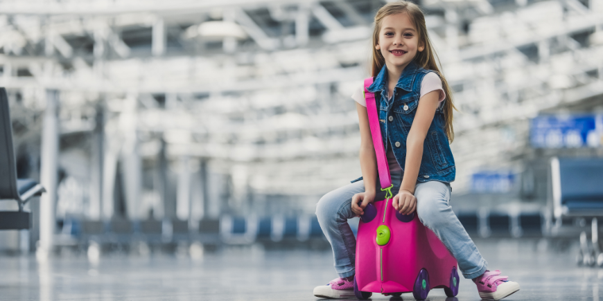 Kind sitzt am Flughafen auf einem Koffer