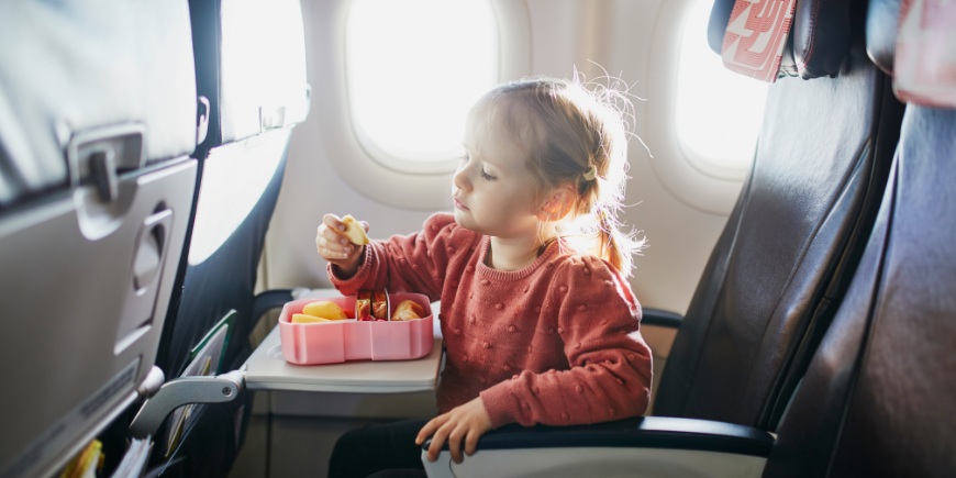 Kind isst auf dem Sitz im Flugzeug einen Snack