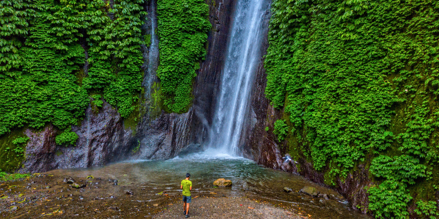 Ein Mann steht am Fuße des Red Coral-Wasserfalls in Munduk, Bali