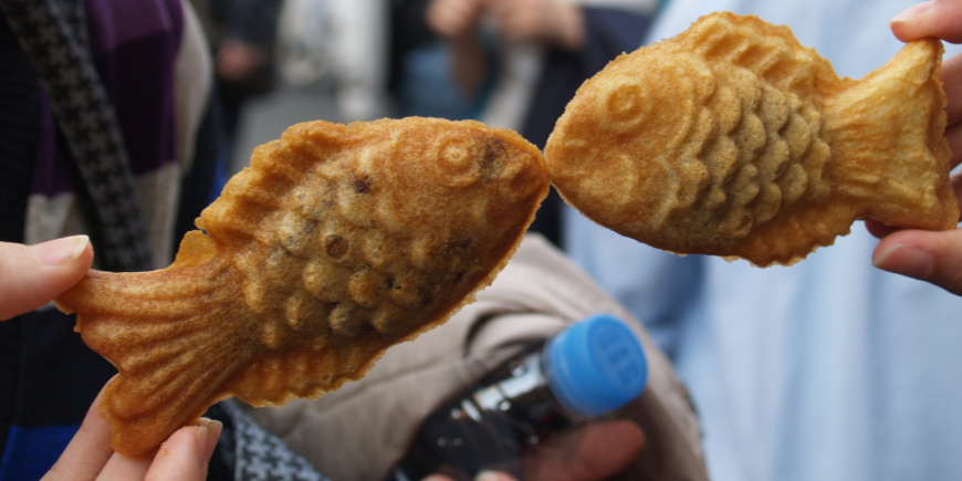 Zwei Menschen halten Taiyaki-Kuchen, sodass es aussieht, als ob Fische sich küssen