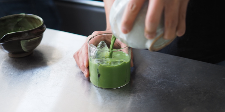 Person hält ein Glas Matcha-Tee hoch