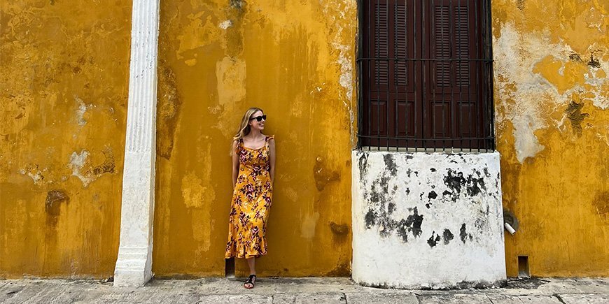 Frau in orangefarbenem Kleid lehnt an einer orangefarbenen Wand in Izamal, Mexiko.