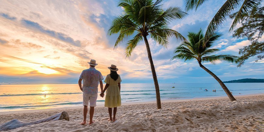 Paar hält sich an den Händen und beobachtet den Sonnenuntergang am Strand von Phuket