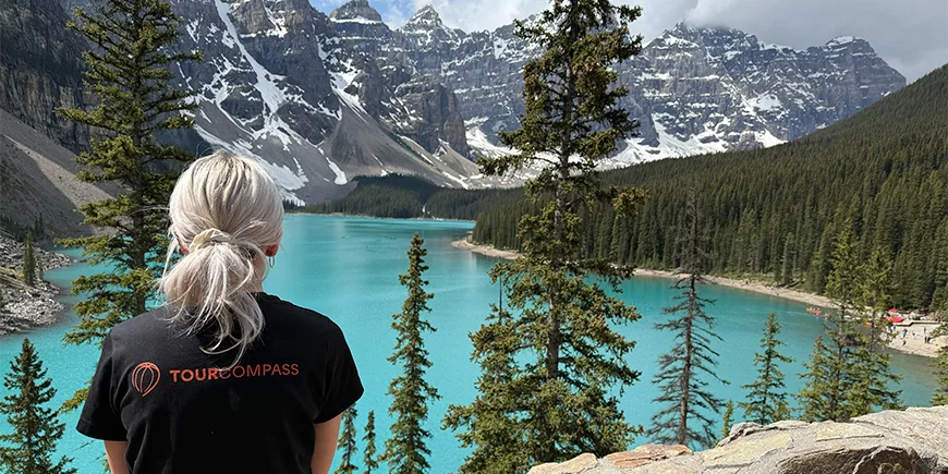 Frau in einem TourCompass-T-Shirt blickt über das Wasser am Lake Louise in Kanada