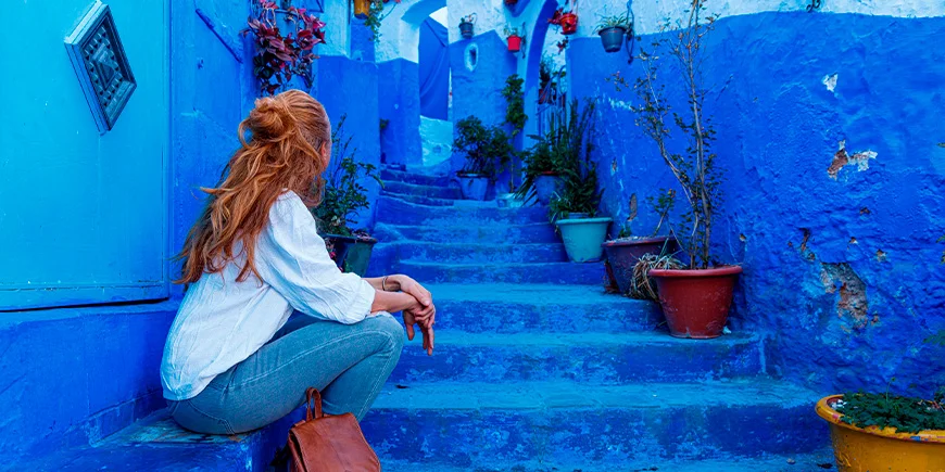 Frau sitzt auf einer Treppe in der blauen Stadt Chefchaouen in Marokko