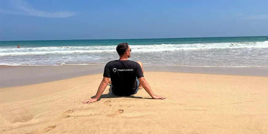 Ein Mann im TourCompass-T-Shirt sitzt am Strand in Mirissa, Sri Lanka