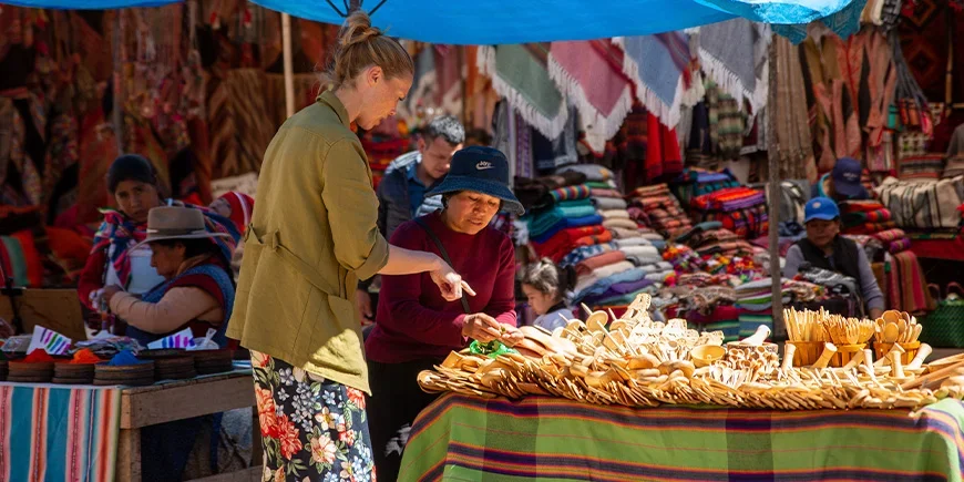 Frau spricht mit einer Einheimischen über die von ihr auf einem Markt in Cusco, Peru, verkauften Souvenirs
