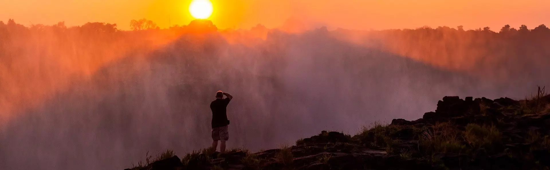 Mann fotografiert in der Dämmerung die Victoriafälle