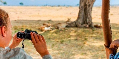 Mädchen auf Safari in Kenia mit Löwen im Hintergrund.